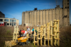 In the foreground are students working on their structure, with a tall grain elevator visible in the background. 