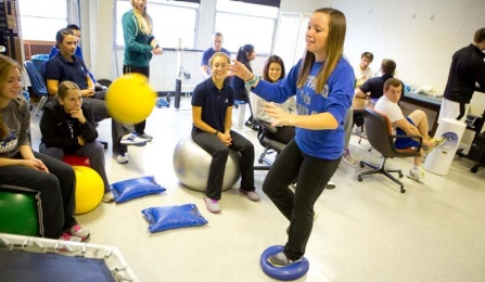 A student performing a balance exercise while other students look on. 