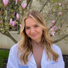 DPT student Madison Schneeberger under a magnolia tree in her white coat. 